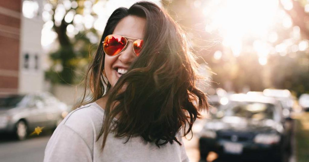 Close up of woman wearing sunglasses standing in the street with the sun beaming behind her
