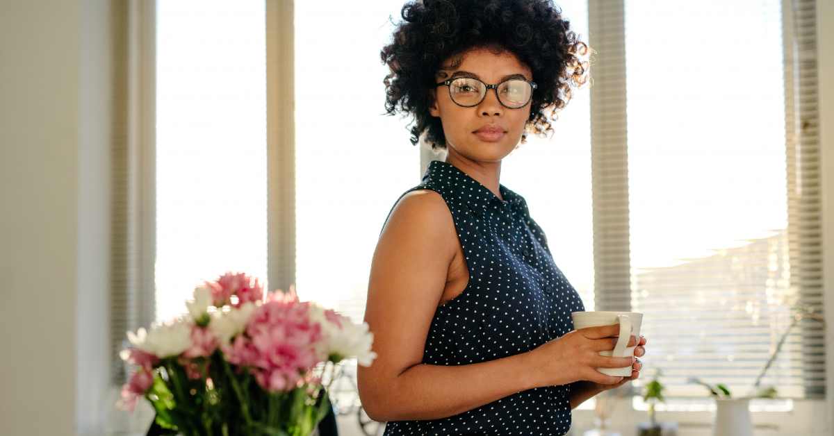 Woman wearing glasses and holding a coffee mug while looking at the camera