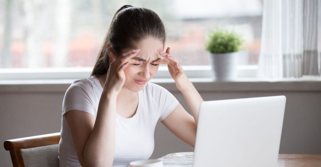 a woman holding her head in front of a laptop
